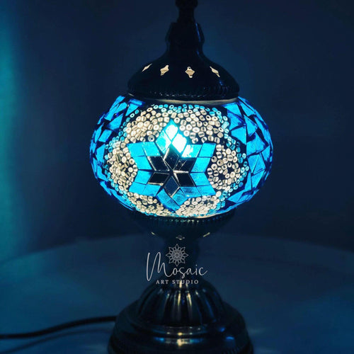 Turkish mosaic lamp with blue star pattern glowing softly on black metal base in dark room