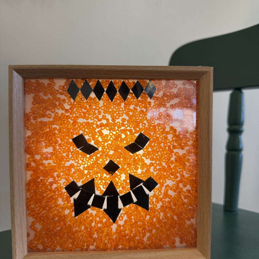 Handmade jack-o'-lantern mosaic light box with a black glass carved face on orange beads in a wooden frame