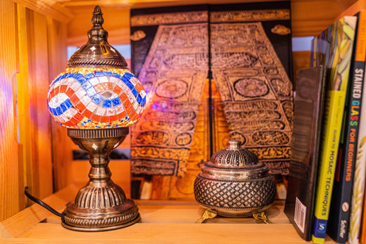 Decorative mosaic lamp and ornate metal container on a wooden shelf with craft books and artwork