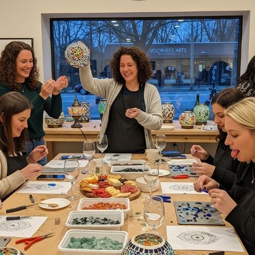 Group of women enjoying a mosaic art workshop with colorful glass pieces and snacks in Voorhees arts studio