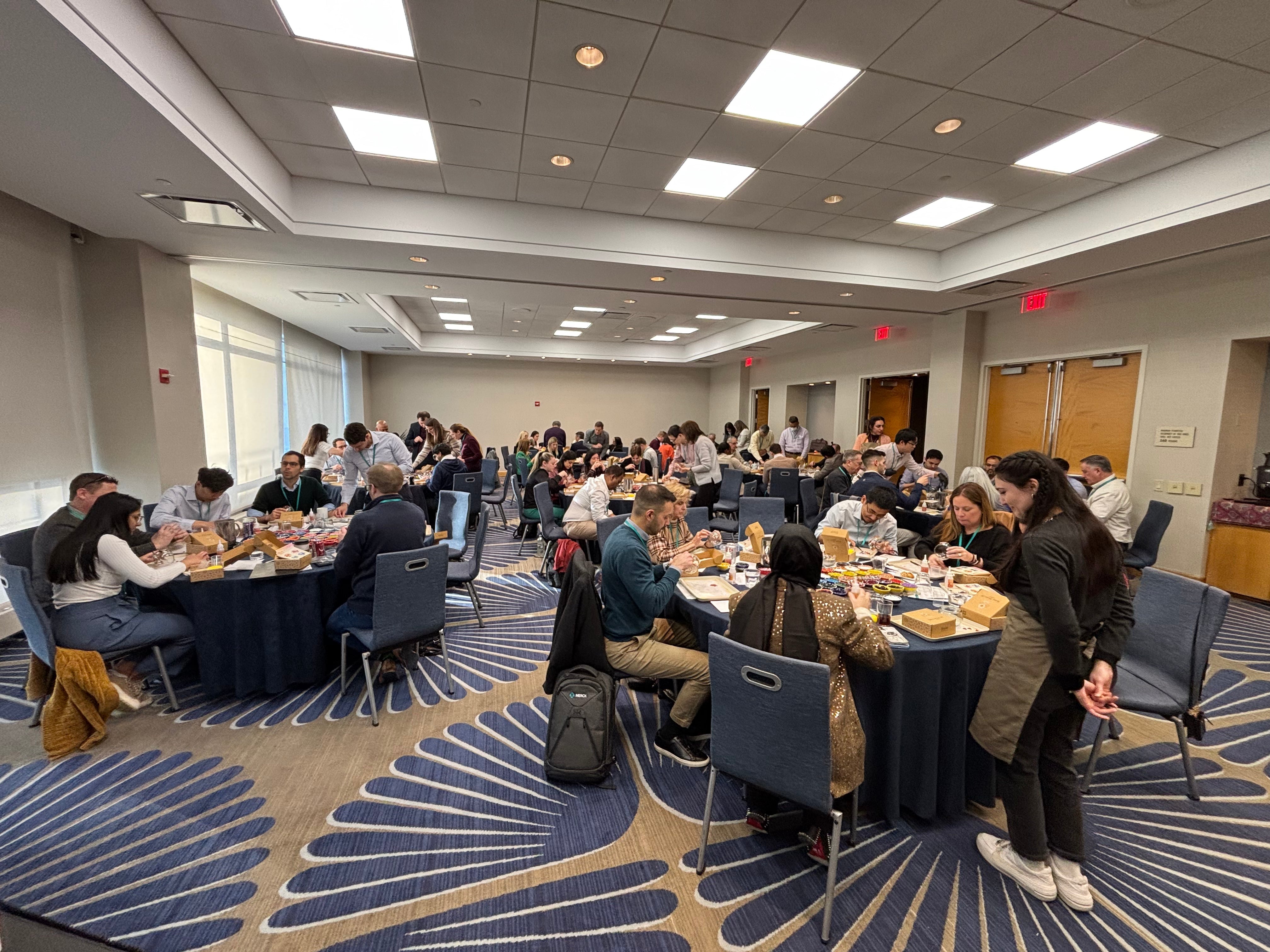 Group of people sitting at round tables in conference room engaged in workshop with craft materials