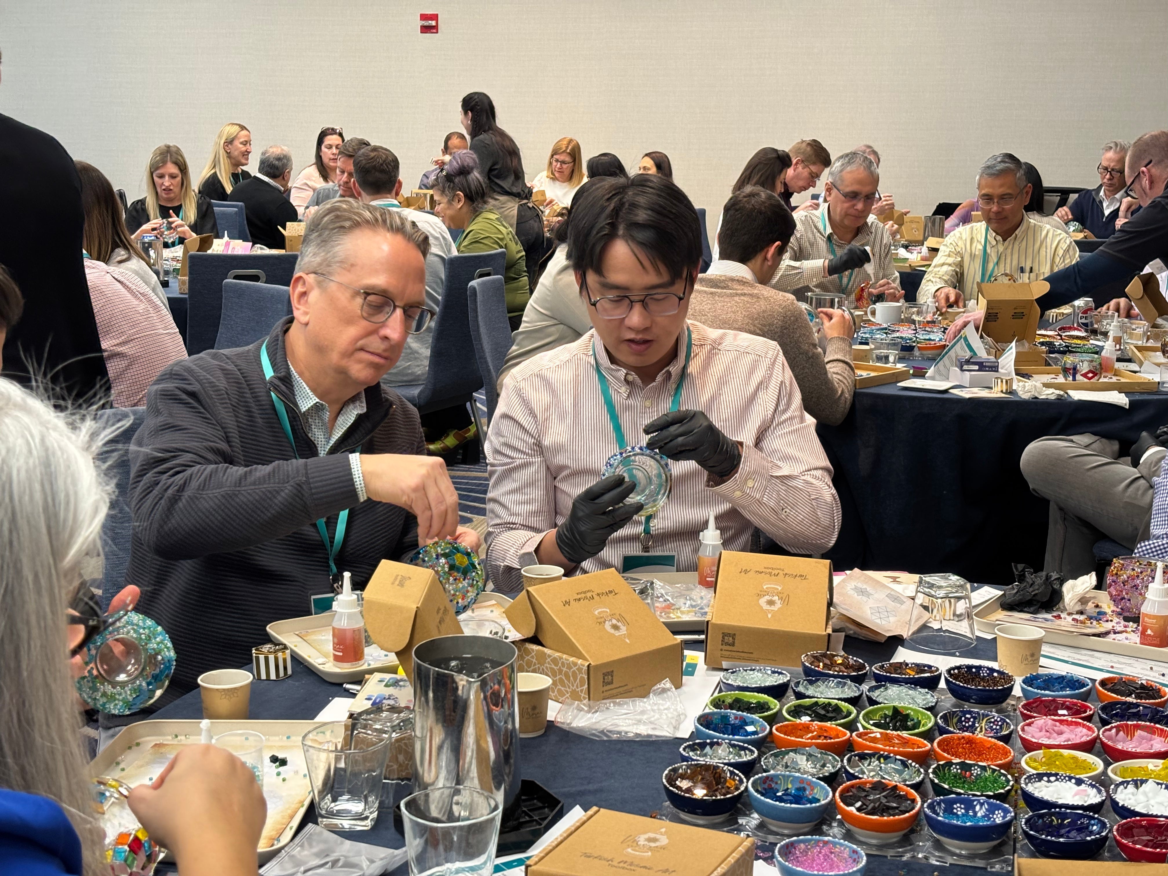 Group of people in a workshop creating mosaic art using colorful glass pieces at tables