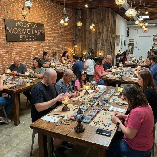 People crafting mosaic lamps at Houston Mosaic Lamp Studio workshop with hanging mosaic lamps overhead