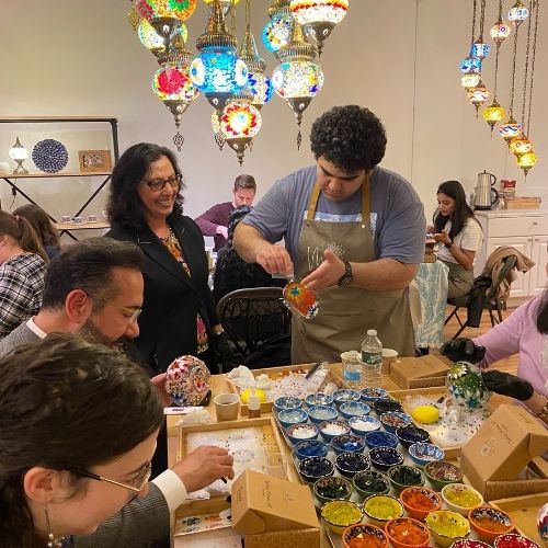 People crafting colorful mosaic lamps in a brightly lit workshop with hanging Turkish lanterns
