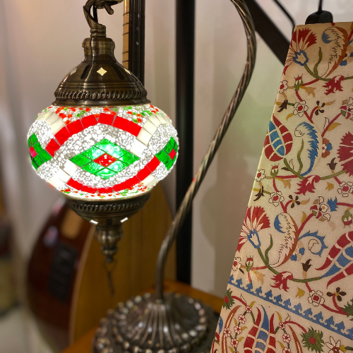 Decorative mosaic table lamp with red, green, and white glass pieces next to colorful floral fabric