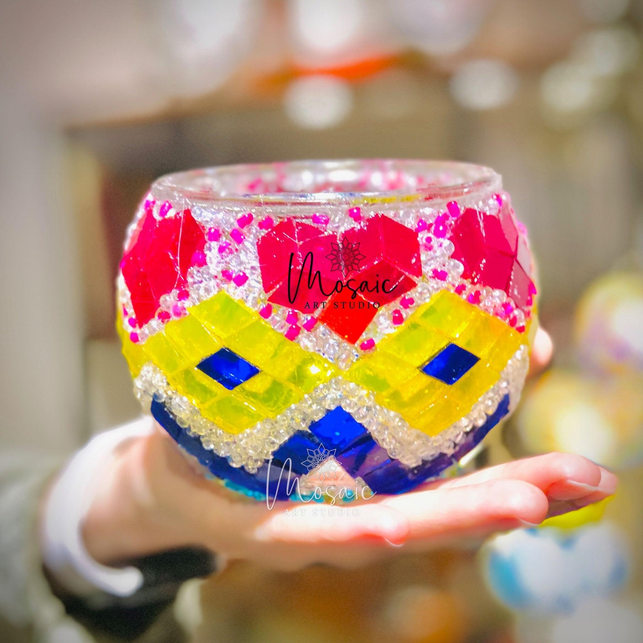 Hand holding a colorful Turkish mosaic glass candle holder with red, yellow, blue, and clear glass pieces