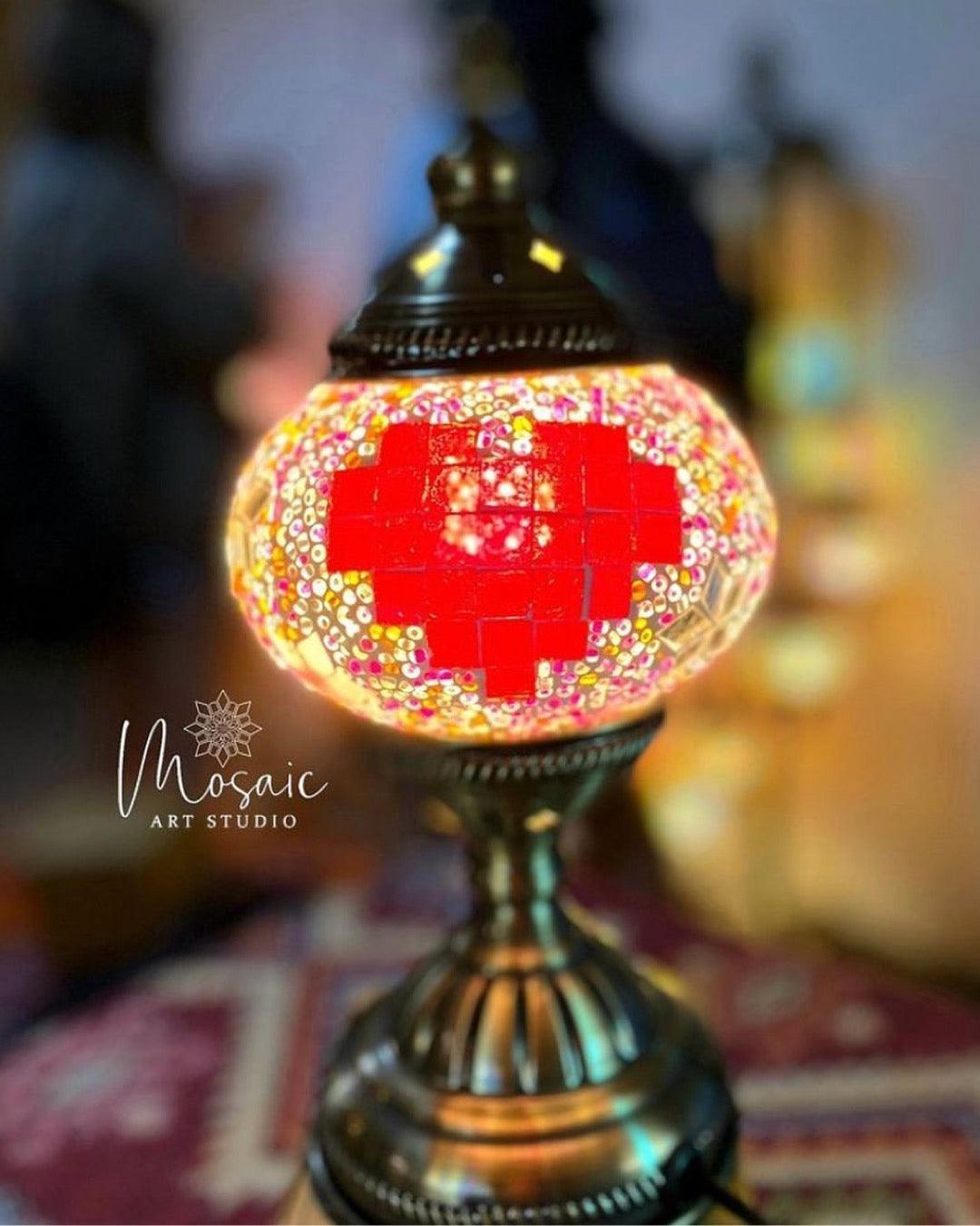 Turkish mosaic lamp with red heart pattern on brass base, glowing warmly indoors