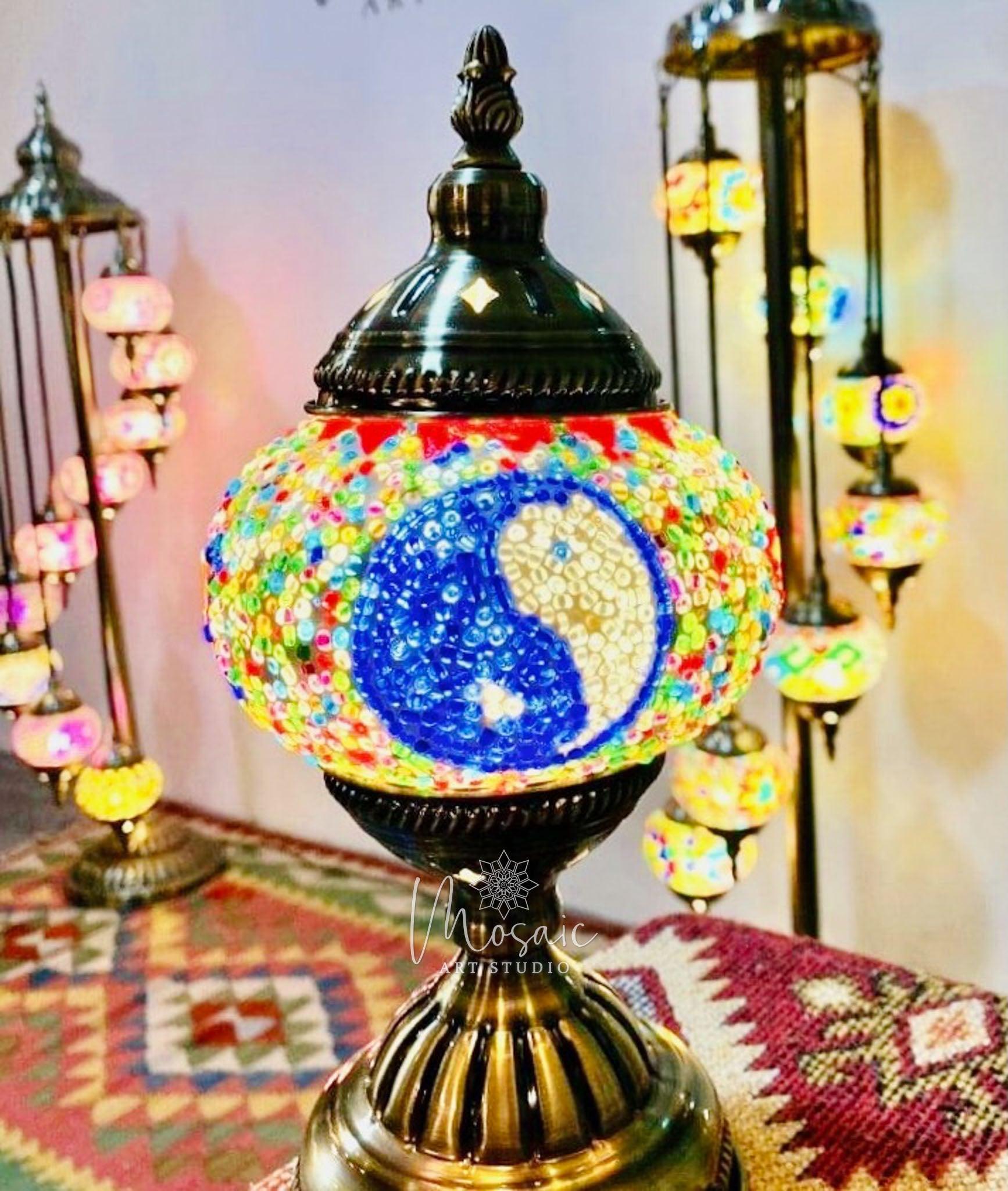 Close-up of a colorful Turkish mosaic lamp featuring a yin-yang pattern, with other mosaic lamps blurred in the background