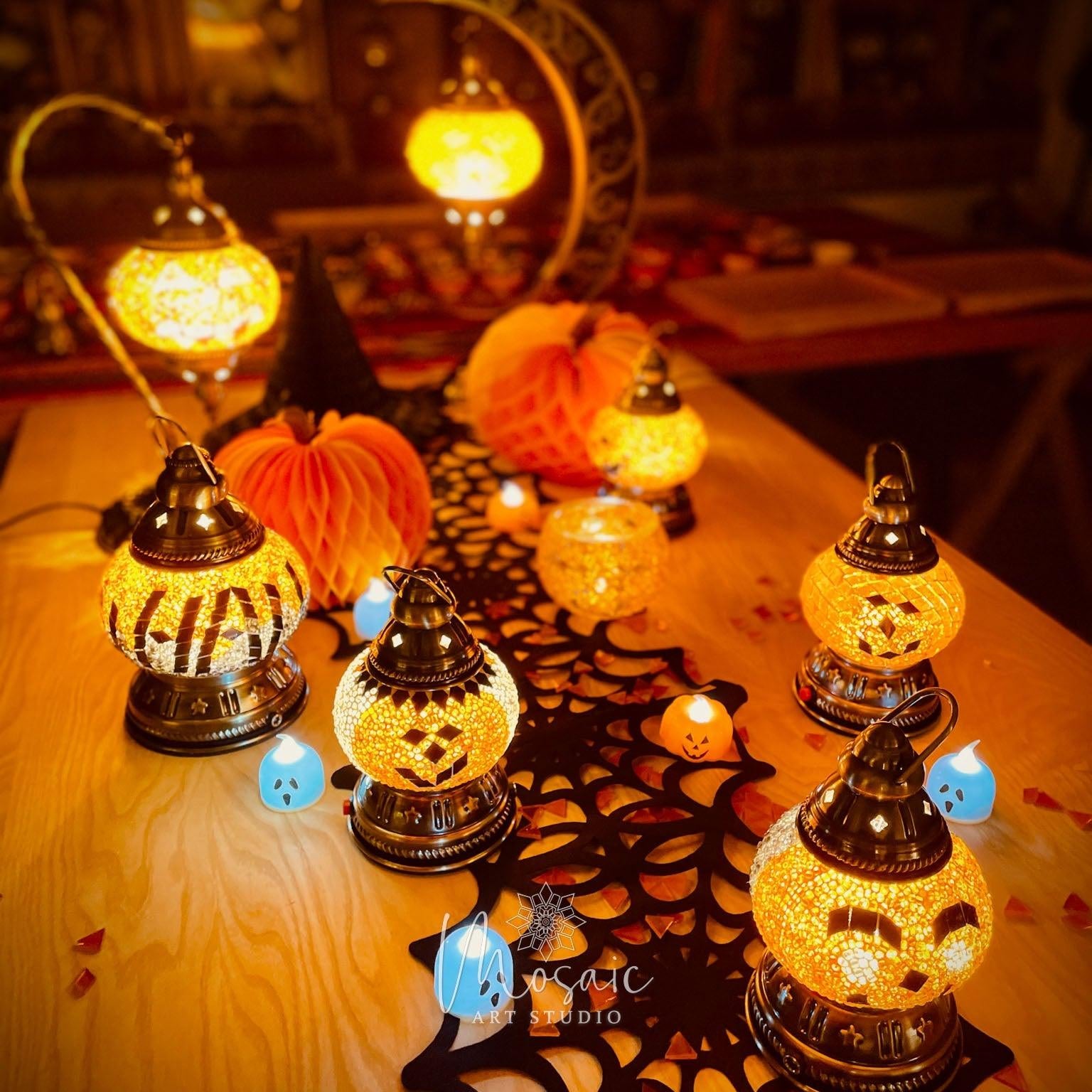 Halloween mosaic lamps with pumpkin faces and warm orange glow on wooden table with black spiderweb cloth