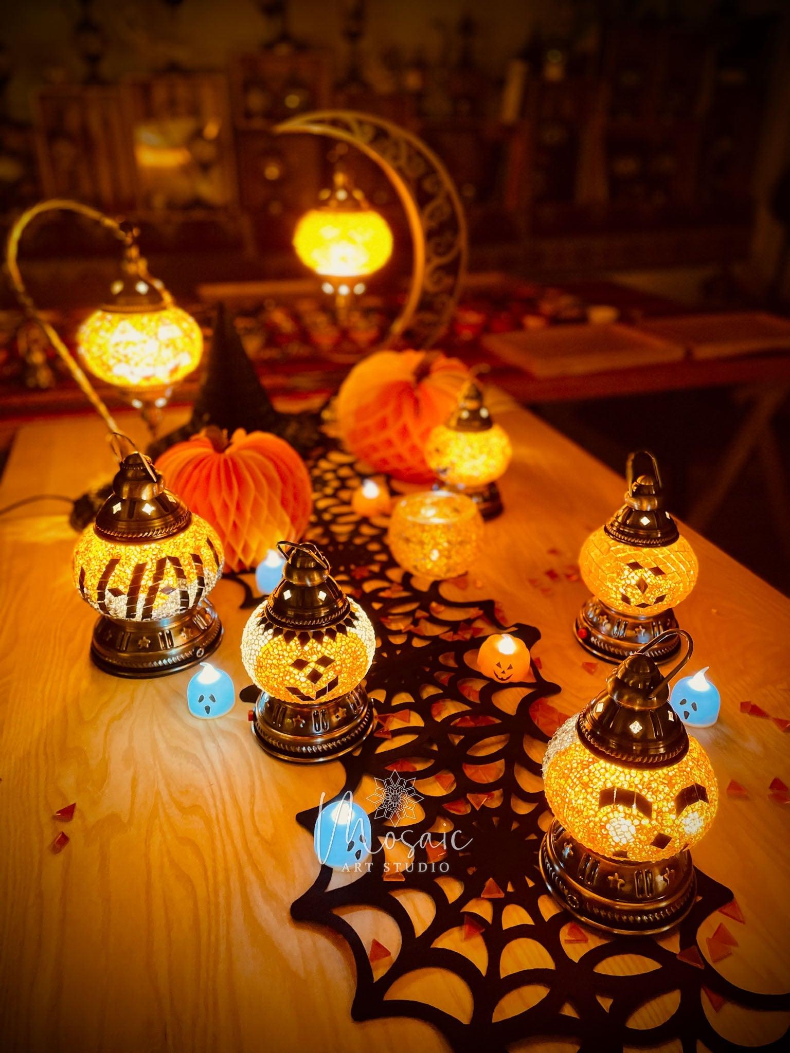 Halloween mosaic lamps with pumpkin faces and warm orange glow on wooden table with black spiderweb cloth