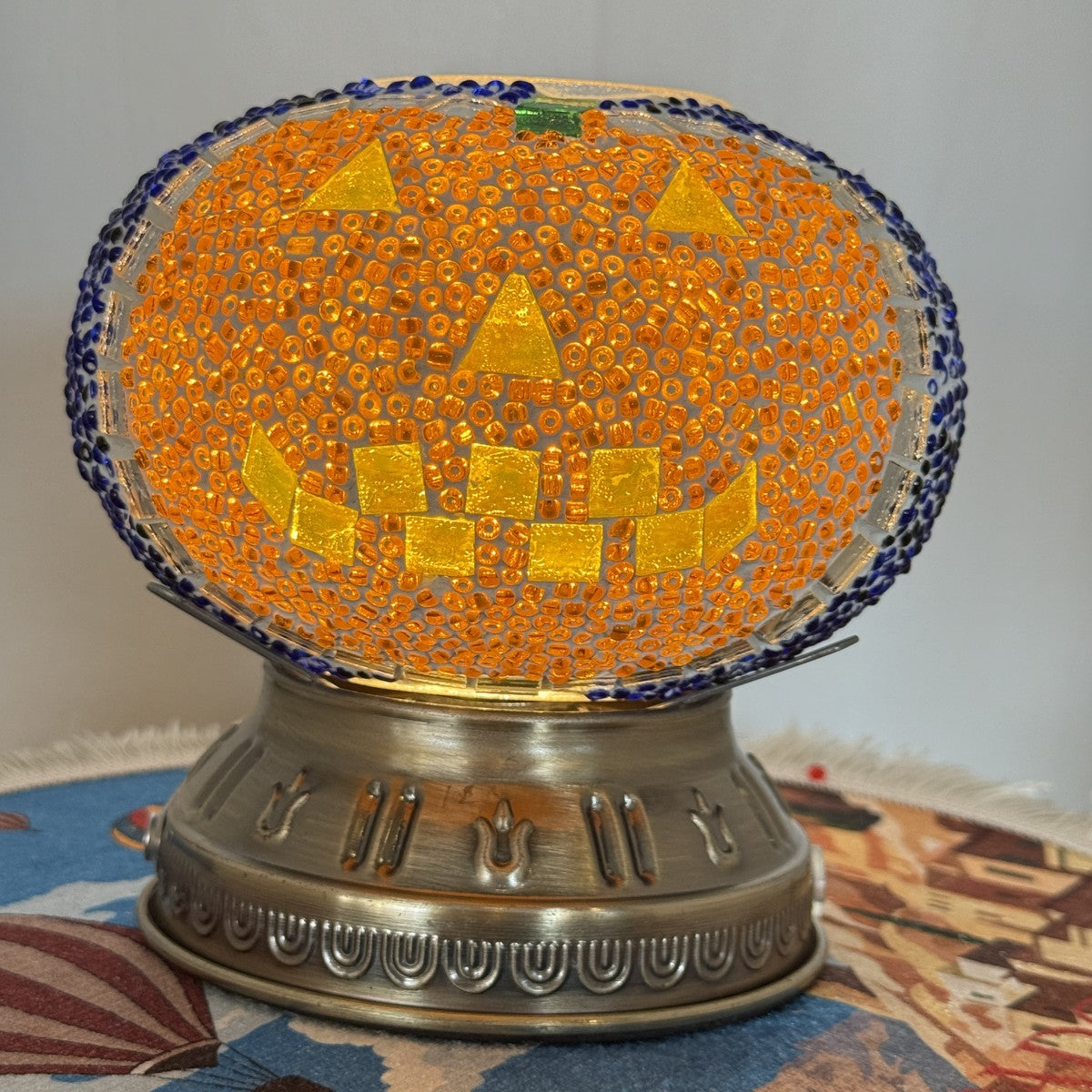 Orange jack-o'-lantern mosaic globe lamp with a cobalt blue beaded rim, lit on a metal base