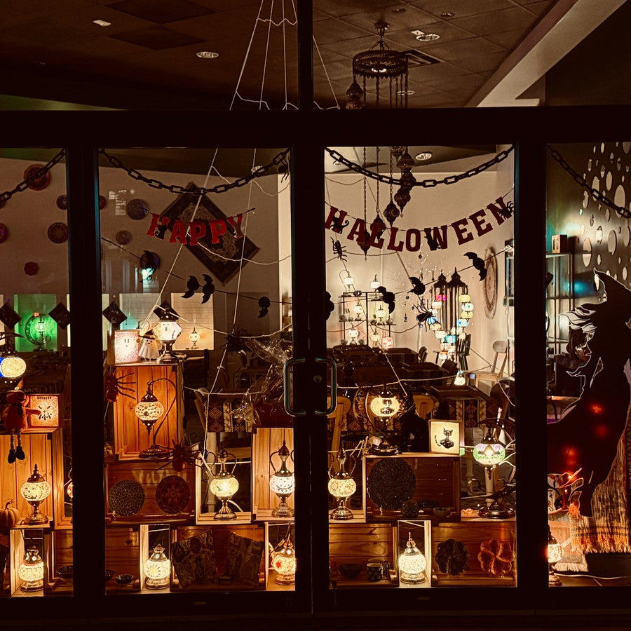Mosaic Art Studio Halloween storefront window at night filled with glowing mosaic lamps and paper garlands