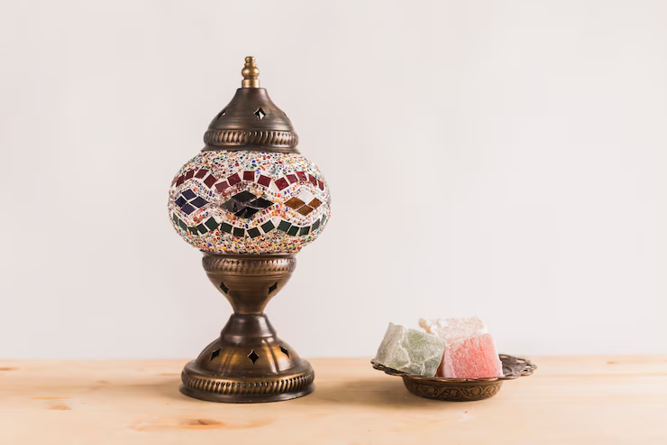 Turkish mosaic lamp with colorful glass pieces and plate of assorted Turkish delight on wooden surface