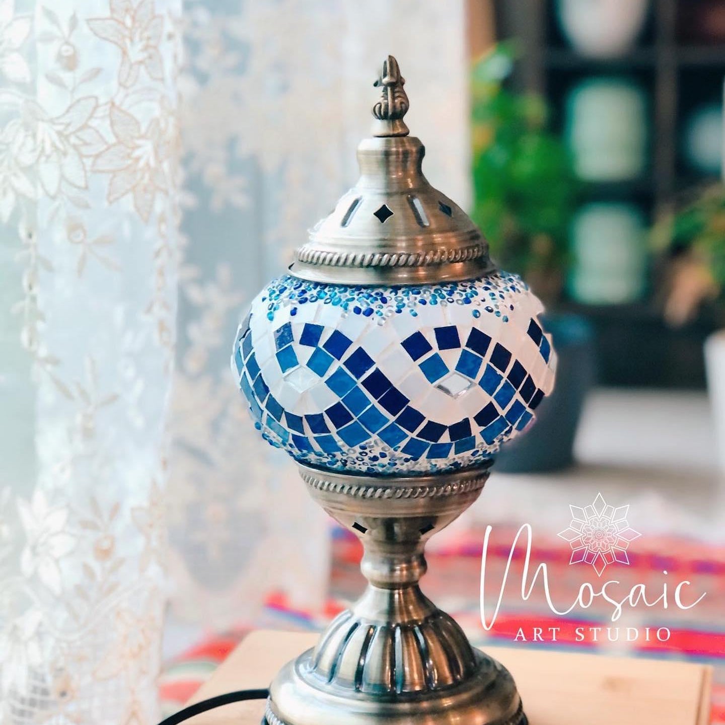 Turkish mosaic lamp with blue and white glass tiles on brass base, displayed on wooden surface