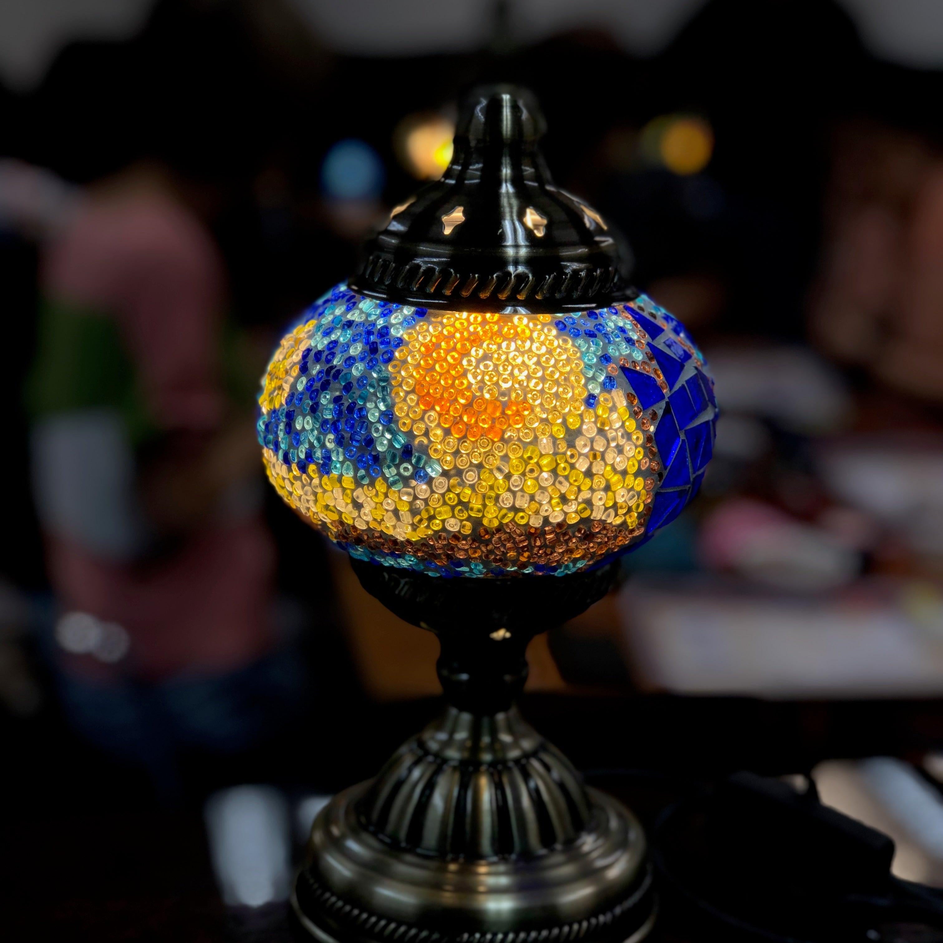 Turkish mosaic lamp with colorful glass beads glowing on a dark metal base in a dim room