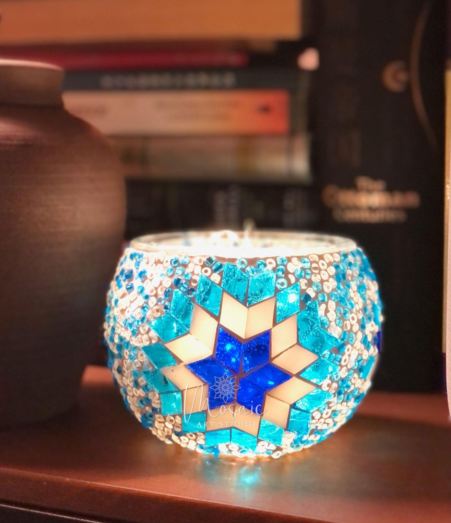 Turkish mosaic lamp with blue star pattern glowing on wooden shelf near pottery and books