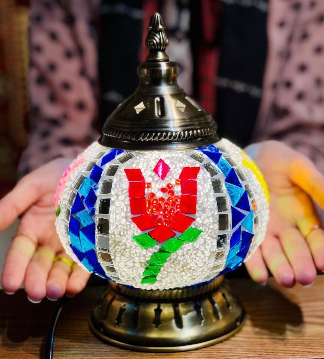 Turkish mosaic lamp with red tulip pattern, blue and yellow glass beads on brass base, held by hands