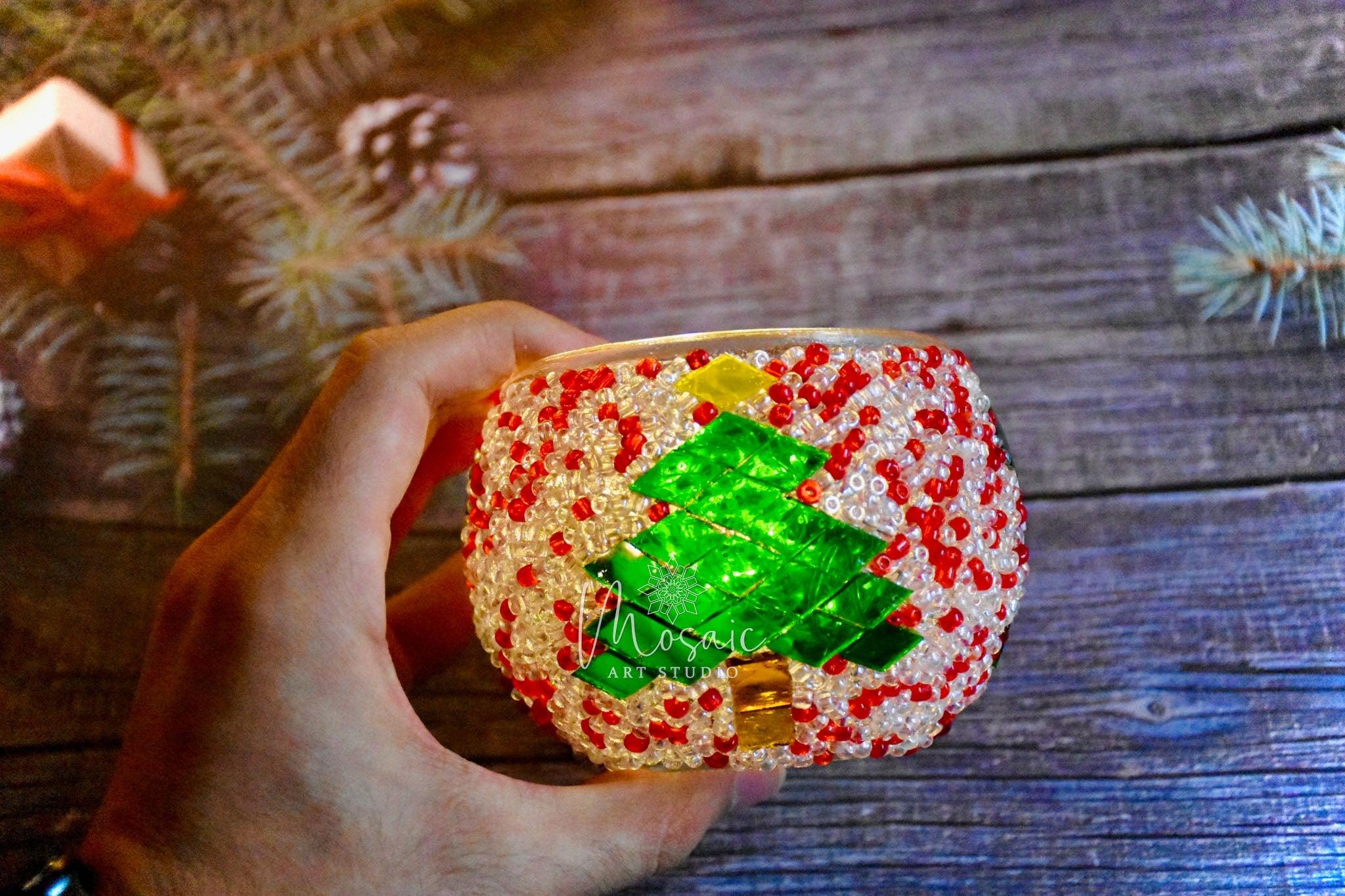 Hand holding beaded Christmas candle holder with red, white beads and green mosaic tree design
