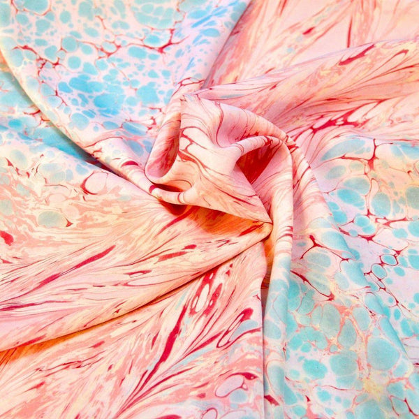 Close-up of marbled fabric with pink, red, and light blue swirl patterns, smoothly folded