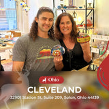 Two smiling people indoors holding colorful mosaic glass lamps in a bright craft studio in Cleveland, Ohio