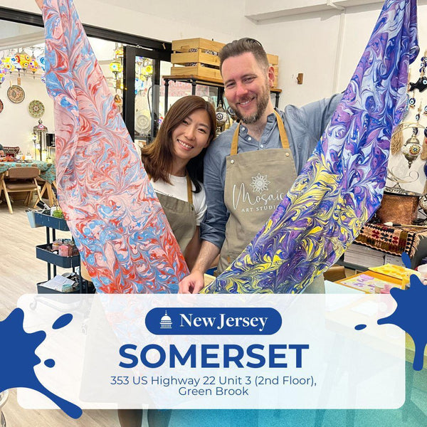 Two artists smiling and holding colorful marbled fabric sheets inside a vibrant art studio in Somerset, New Jersey