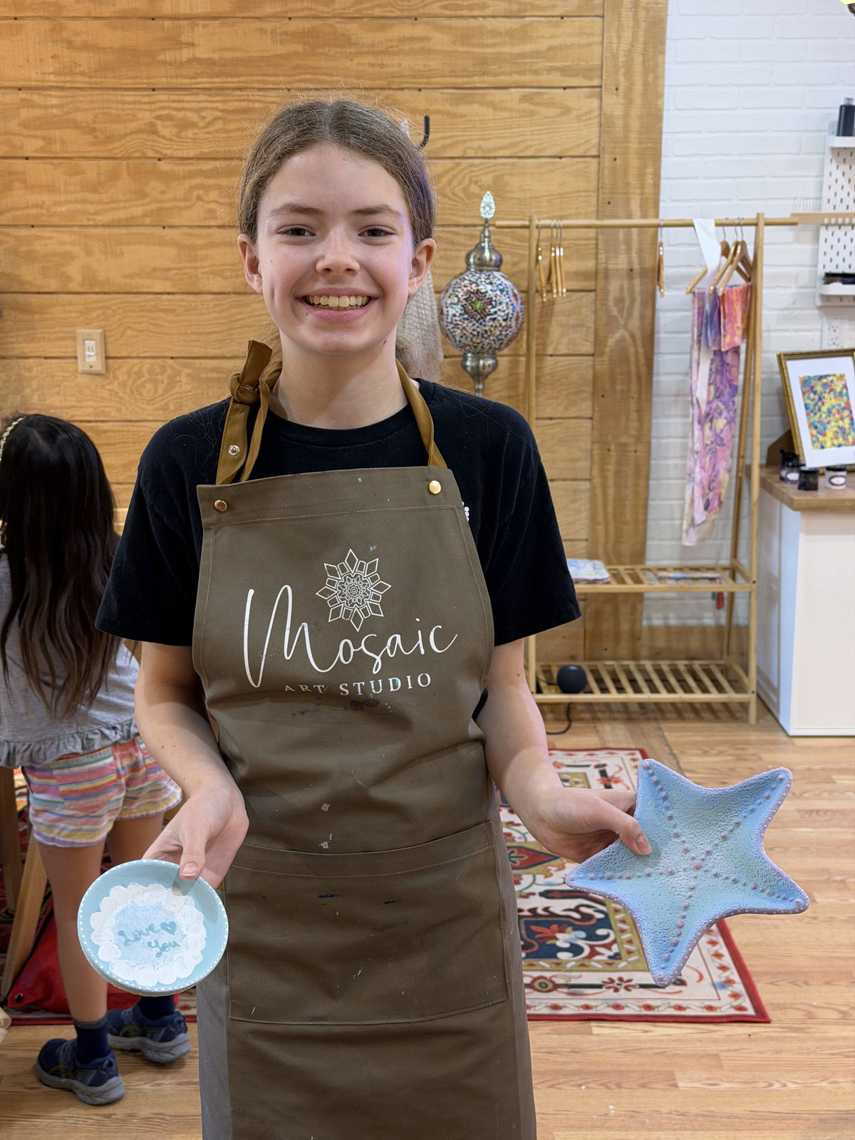 Student in a Mosaic Art Studio apron holding a finished painted ceramic star and plate