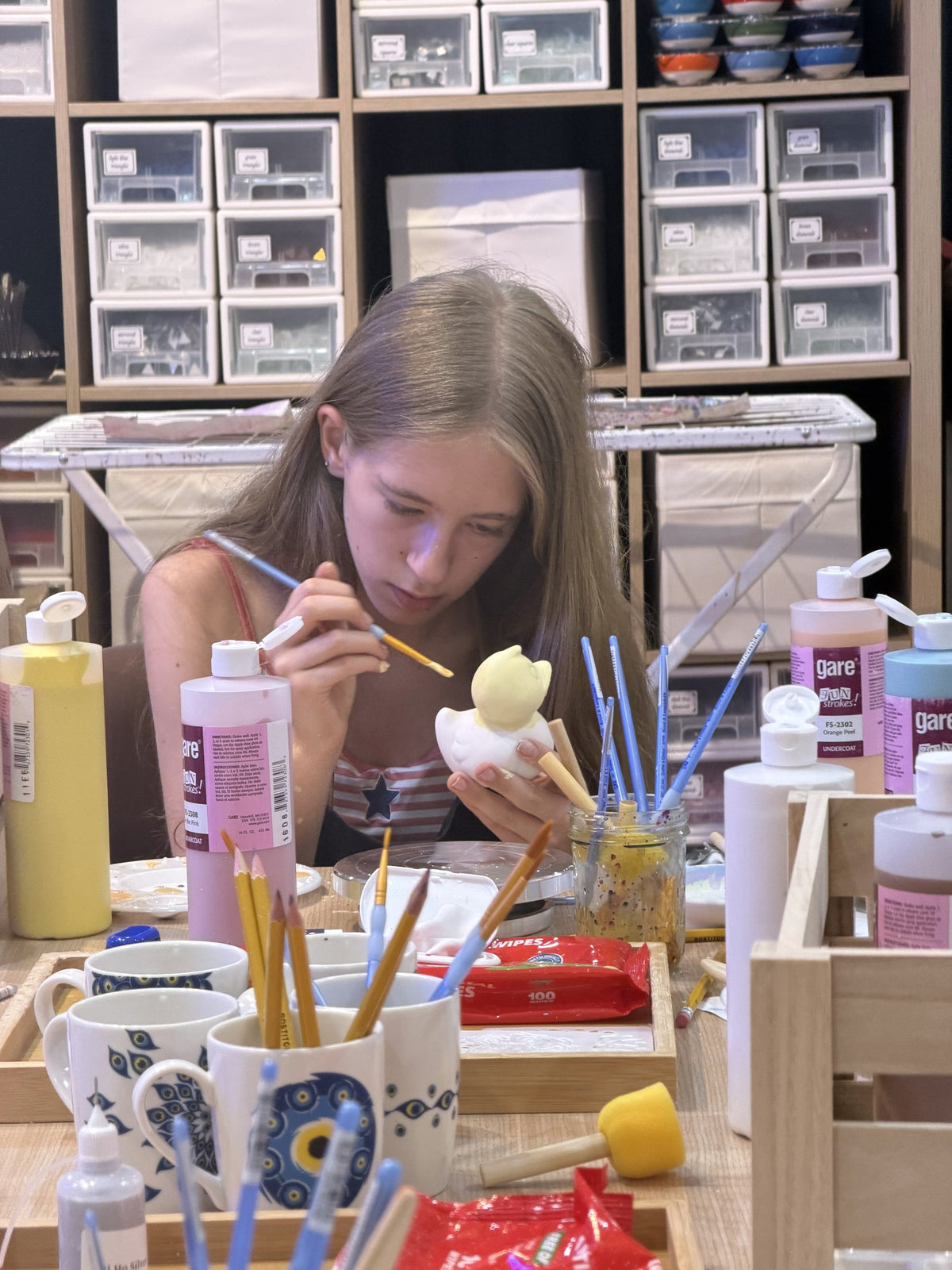 Close-up of a student painting a small ceramic figure with a fine brush