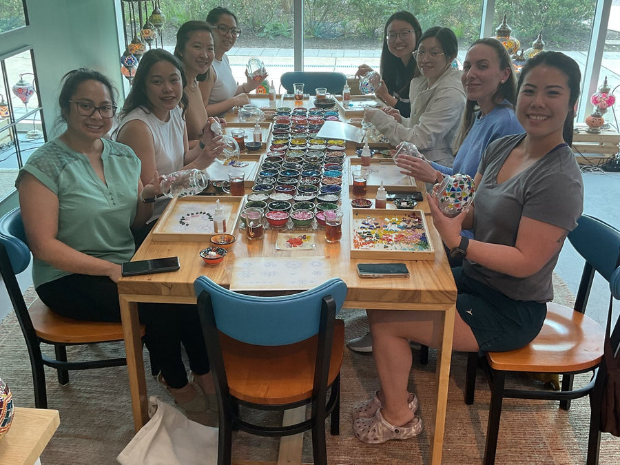 Friends smiling over bowls of mosaic glass at a workshop table in Voorhees, NJ