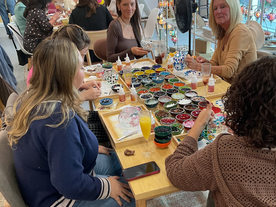 Friends placing colored glass tiles on mosaic lamps at a workshop table in the Voorhees, NJ studio