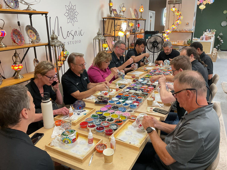 A long table of coworkers making mosaic lamps at a team building event in Voorhees