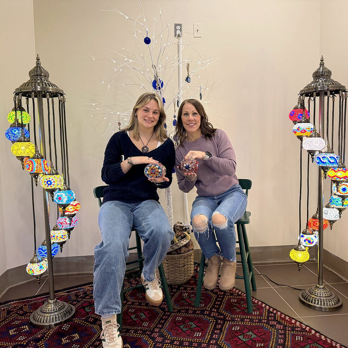 Two friends sitting between glowing lamp stands with their mosaic lamps