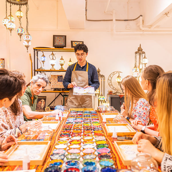 Instructor explaining the mosaic design paper to guests seated around the workshop table