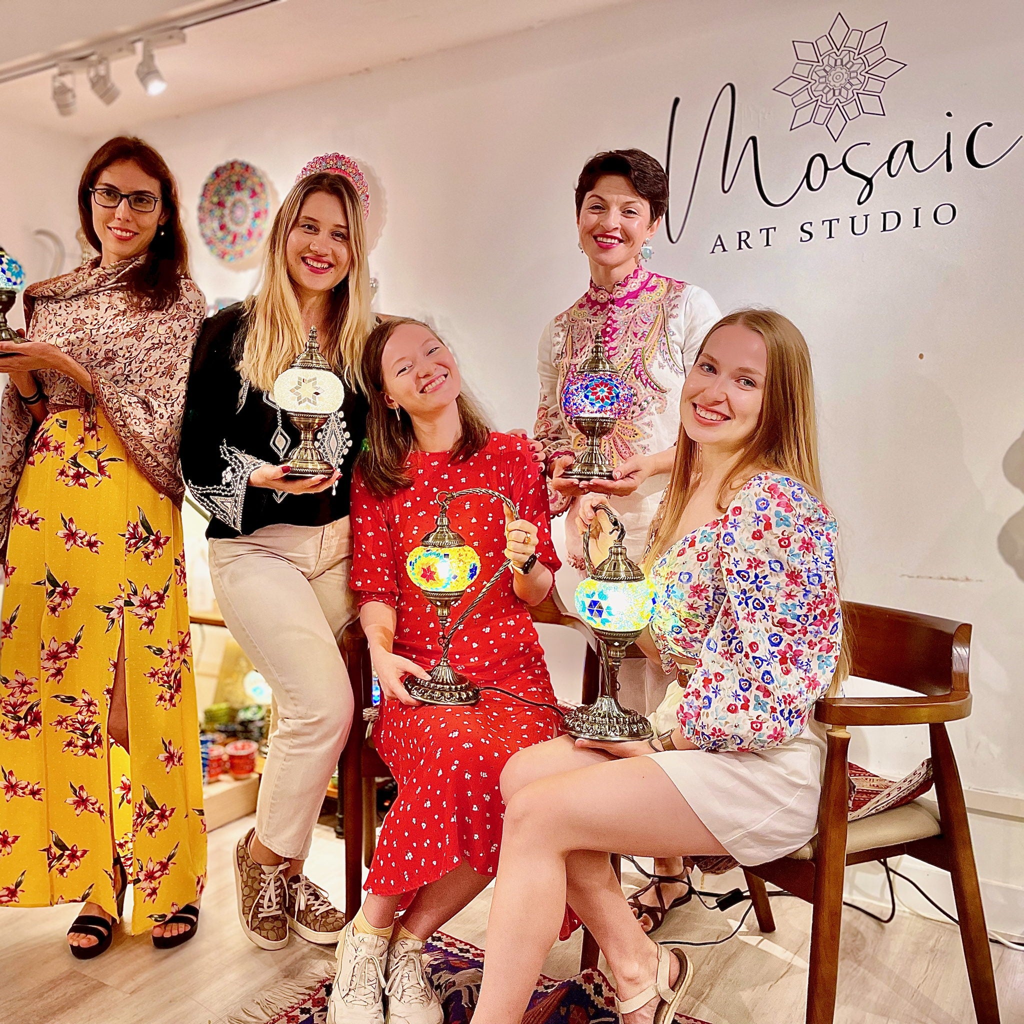 Five guests smiling with their finished Turkish mosaic lamps lit up at the end of a Mosaic Art Studio workshop