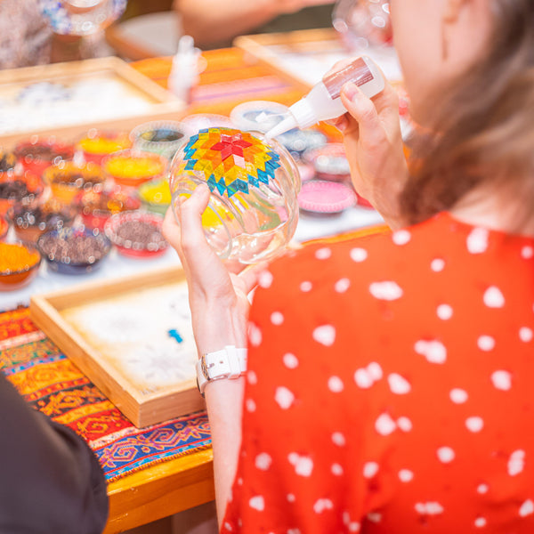 Guest applying glue to a glass lamp globe before placing the next mosaic tiles on a rainbow star pattern