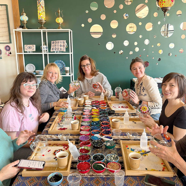 Guests around a long mosaic lamp workshop table with bowls of coloured glass