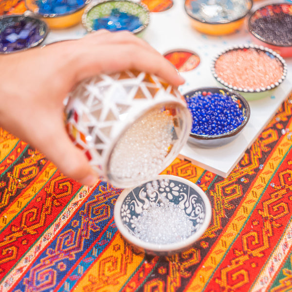 Pouring clear glass beads from a mosaic globe into a bowl while filling the gaps between the patterns