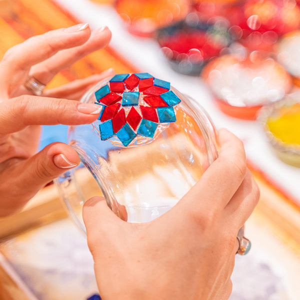 Finished red and turquoise mosaic rosette on a glass lamp globe held in both hands