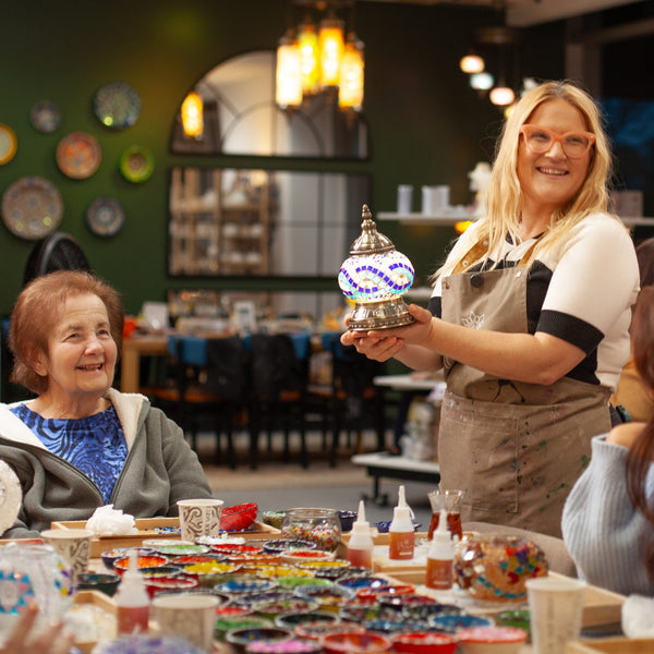 Mosaic workshop table set with bowls of coloured glass tiles, beads and glue as guests take their seats
