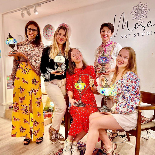 Five women smiling inside mosaic art studio holding colorful mosaic lamps in Voorhees NJ workshop