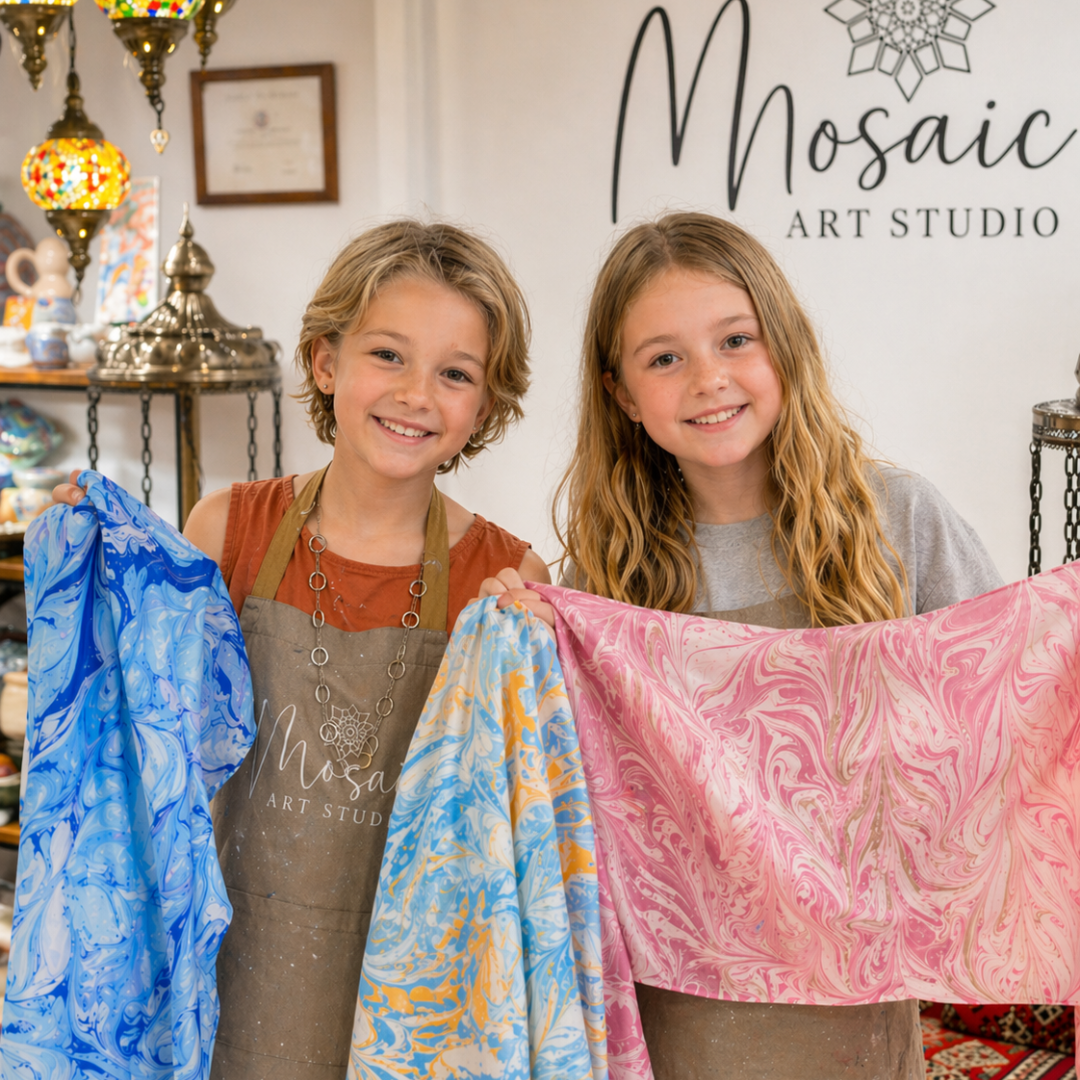 Two smiling kids holding their finished Ebru water marbling artworks at Mosaic Art Studio summer camp