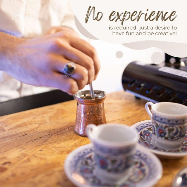 Hand stirring coffee in a copper cezve on wooden table with two ornate Turkish coffee cups