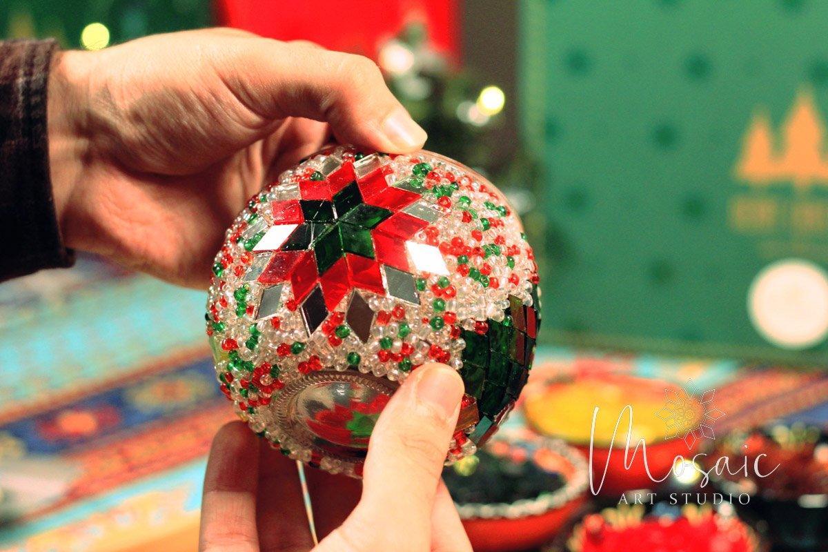 Hands holding a handmade Christmas mosaic candle holder with red, green, and clear beads