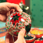 Hands holding a handmade Christmas mosaic candle holder with red, green, and clear beads