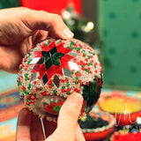 Hands holding a handmade Christmas mosaic candle holder with red, green, and clear beads